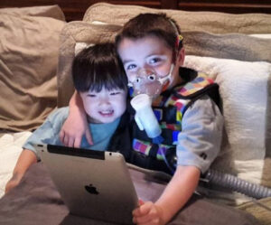 Two small children looking at iPad, one receiving asthma treatment