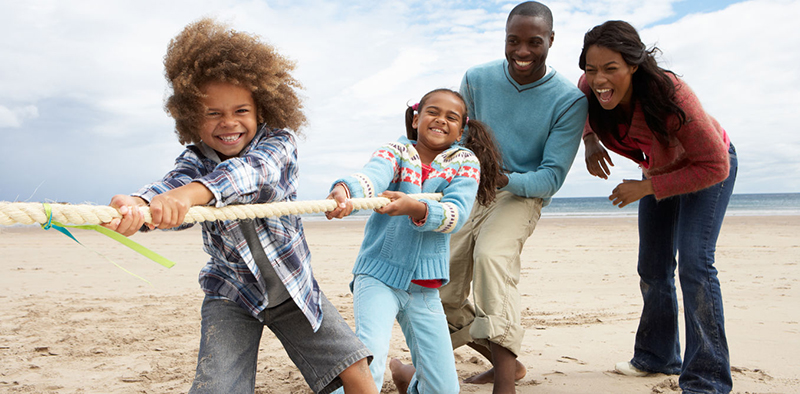African-American family playing tug-of-rope on a beach. A young boy, girl, mother, father.